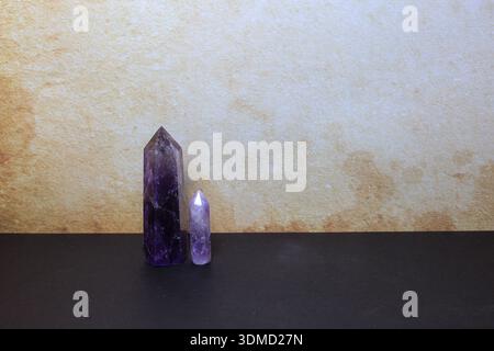 polished amethyst crystal towers in varying sizes, placed vertically on a dark surface with soft beige background. Stock Photo