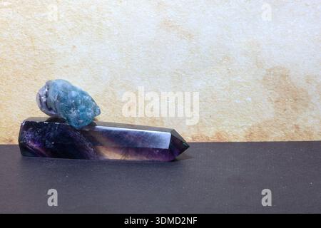 Fluorite stones in raw and polished form displayed on a dark surface, with vivid bands of purple and green visible in the crystal wand. Stock Photo
