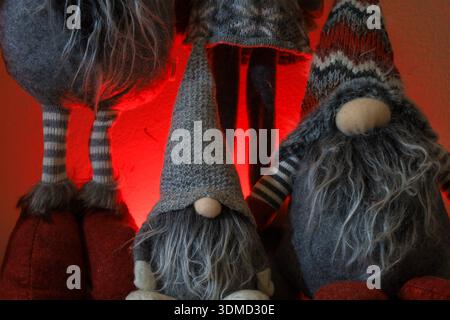 Festive handmade gnome decorations with long beards, striped legs, and textured woolen hats, illuminated by a warm red light in the background. Stock Photo
