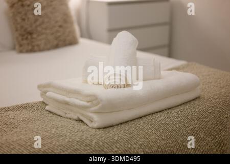Three white towels are stacked on top of each other on a bed. The towels are neatly folded and arranged in a way that they look like they are ready to Stock Photo