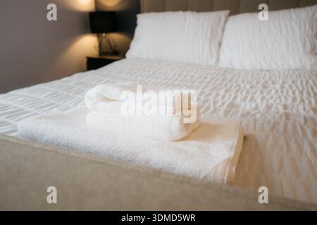 A bed with white sheets and a stack of white towels on top of it. The towels are neatly folded and arranged in a pyramid shape. The bed is well made a Stock Photo