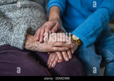 Elderly woman holding hands with her caregiver in a nursing home, close-up Stock Photo