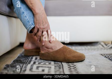 Senior woman suffering from ankle pain while sitting on sofa at home Stock Photo