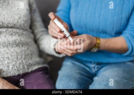 Close-up woman helping her mother check blood sugar level using a 			blood glucose meter at home Stock Photo