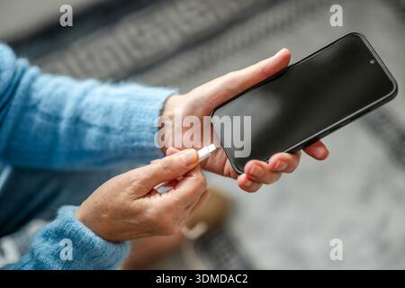 Mature woman connecting USB cable to her smart phone Stock Photo