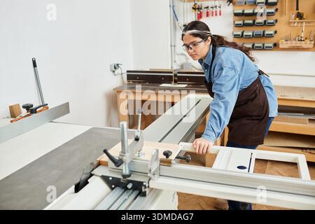Beautiful young woman skillfully working with wood, engaging in her craft with focus and joy. Stock Photo