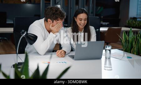 Joyous Caucasian business managers talking smiling laughing with laptop successful partnership in company businessman with businesswoman talk laugh Stock Photo