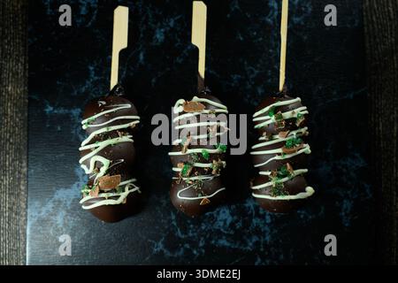 Three chocolate covered donuts with green sprinkles on top. The donuts are sitting on a black table Stock Photo