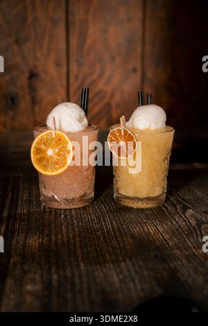 Two glasses of cocktails with ice and fruit garnish on the table. One is pink and the other is yellow Stock Photo