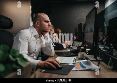 Focused businessman at desk reviewing charts on multiple screens in a modern office Stock Photo