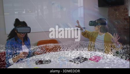 Exploring two women wearing mustard cardigan and VR headsets manipulating data at meeting table Stock Photo