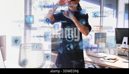 Standing woman wearing dark business dress and smart glasses using AR interface in office, laptop Stock Photo