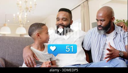 Smiling family trio sitting close on gray sofa in bright living room, with white heart overlay Stock Photo