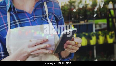 Checking nursery worker in blue plaid shirt, apron, using phone, receipt or pencil, candlestick char Stock Photo