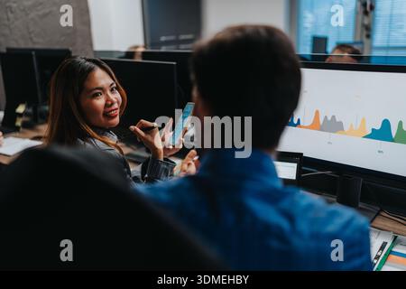 Business team collaborates in an office, discussing data on a monitor and smartphone Stock Photo