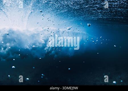 Underwater view of breaking ocean wave, blue water with sun light rays and bubbles Stock Photo