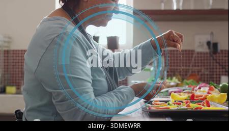 Sprinkling Indian cook in dark-apron at counter salting pepper tray with blue overlay, copy space Stock Photo