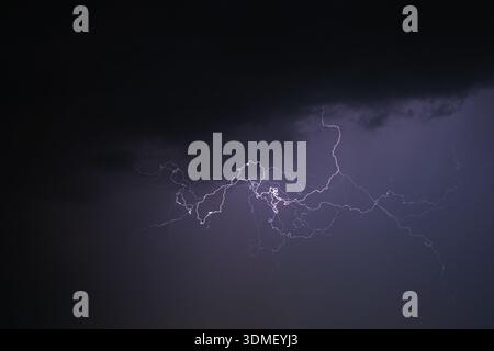Powerful lightning strikes across a dark stormy sky with purple hue Stock Photo