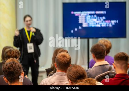 Audience listens to speaker during tech talk as code appears on screen. Stock Photo