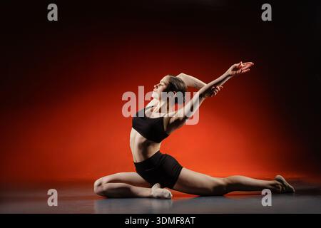 Full length woman doing floor split stretch with backbend in studio on red gradient background with copy space for a fitness website banner or social Stock Photo
