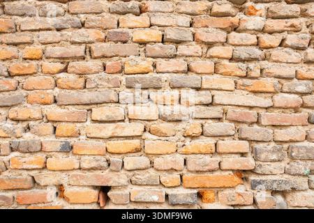 A rustic brick wall shows weathered orange, tan, and gray bricks with rough surfaces. Ideal for architecture, design, or urban mood projects seeking t Stock Photo