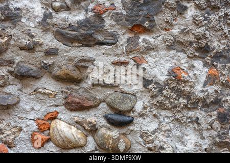 A weathered stone wall embedded with pebbles, bricks, and dusty mortar. The rough texture and mixed colors evoke rustic outdoor construction, aging ar Stock Photo