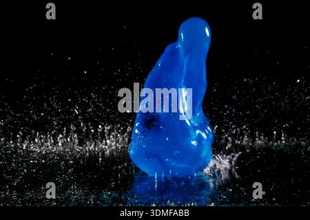 Deformed water balloon hitting a glass plate wetted with water against a dark background. Stock Photo