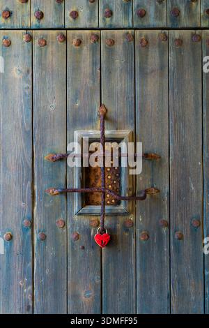 Small window on old wooden wall with rusty metal grille. Red heart-shaped padlock hanging on grille, symbol of love, fidelity, romance and emotional c Stock Photo