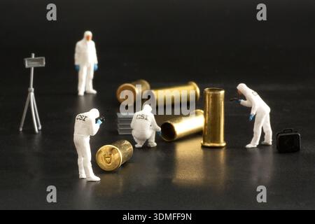 Miniature forensic investigators examine cartridge cases in a studio crime scene illustration. Stock Photo