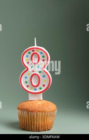 Birthday cupcake with number 8 candle decorated with colorful polka dots on a neutral background Stock Photo