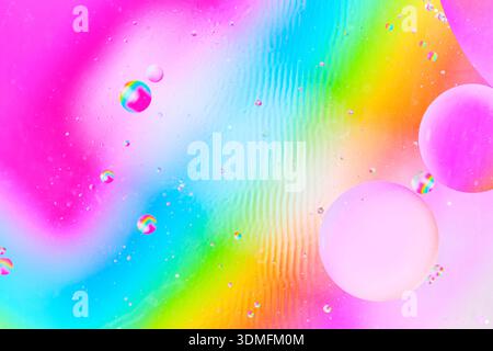 Multicolored abstract macro of oil spheres on rainbow gradient background with liquid ripples Stock Photo