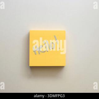 High-quality photograph of a yellow post-it note with the word "Hello" written on it, placed on a clean white table. Perfect for office photography, e Stock Photo