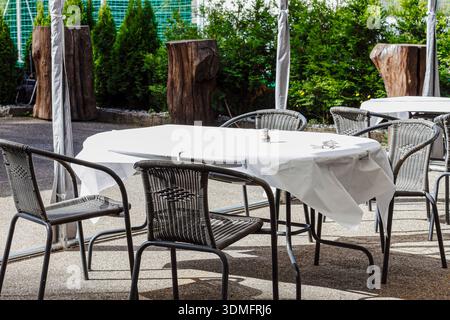 Empty tables with white tablecloths and black chairs in an outdoor terrace of a cozy summer cafe. Stock Photo