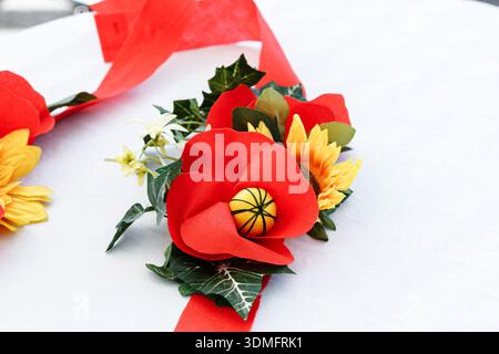 Artificial flower arrangement with red poppies and yellow sunflowers on a white table for festive decoration. Stock Photo