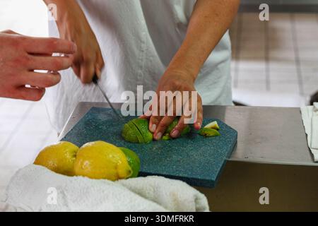 Hands of a chef slicing fresh green limes and lemons on a cutting board in a professional kitchen. Stock Photo