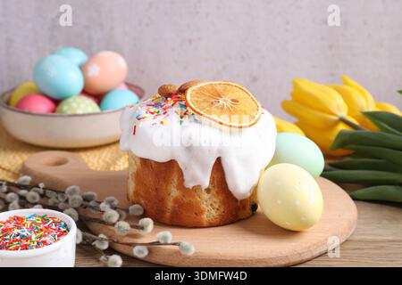 Delicious Easter cake with sprinkles, painted eggs, willow branches and tulips on table against gray background, closeup Stock Photo