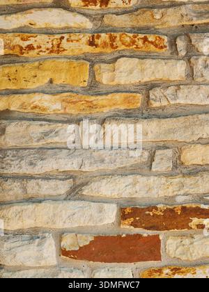 Natural stone wall with irregularly shaped stones in beige, gray, and brown shades. Gray mortar highlights the structure. Rough and rustic. Close-up. Stock Photo