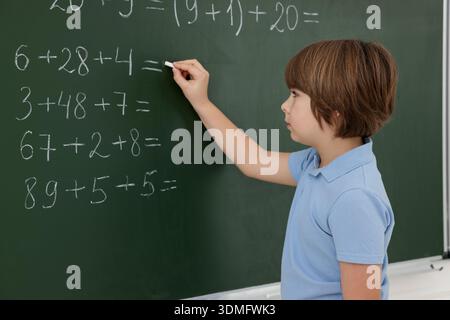 Schoolboy doing math on chalkboard in classroom Stock Photo