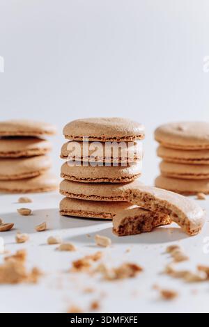 Stacked peanut macarons with bitten cookie and crumbs on white background Stock Photo