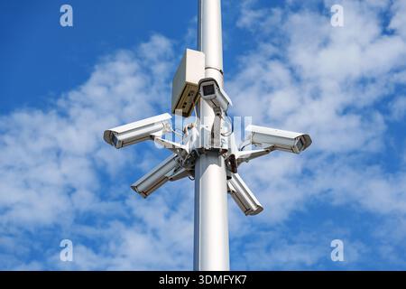 Multiple surveillance cameras mounted on a tall pole against a blue sky for area monitoring Stock Photo