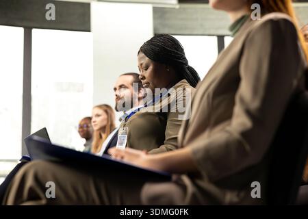 African american female attendee writes ideas on laptop at conference, business forum event with panel discussion and speaker. Multiracial audience takes notes for entrepreneurship. Stock Photo
