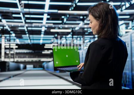 Green screen laptop used by developer in data center managing server virtualization. IT staff member using chroma key notebook in server hub, doing upgrades sustaining long term equipment reliability Stock Photo