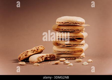 Stacked beige macarons with crumbs and peanuts on brown background copy space Stock Photo