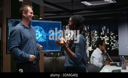 Silicon Valley company IT staff members laughing in office, developing apps with AI. System administrators sharing jokes while waiting for artificial intelligence to debug applications Stock Photo