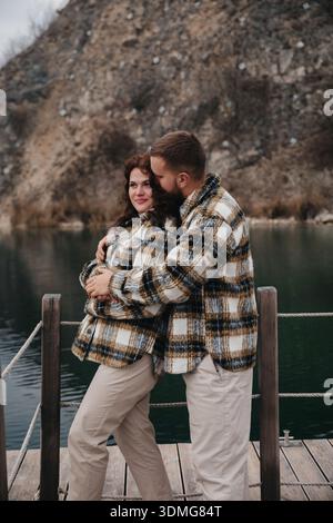 Man and woman stand close to each other on a dock by the water. They are smiling and wearing matching jackets. Stock Photo