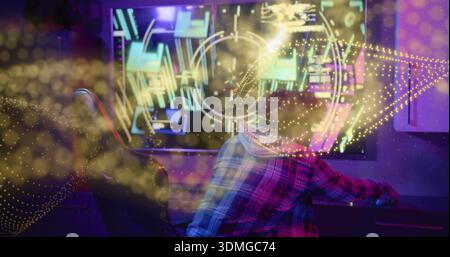 Leaning man wearing plaid flannel hoodie focusing on monitor in home studio with neon HUD, keyboard Stock Photo