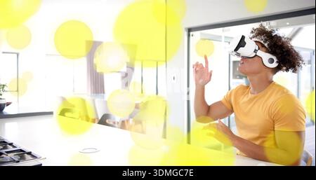 Wearing white VR headset, man in yellow tee exploring overlays at kitchen counter, copy space Stock Photo