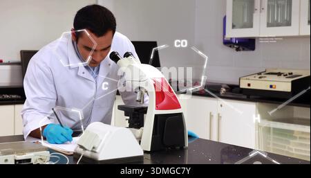 Researcher in white lab coat and blue gloves using microscope, taking notes at lab with overlays Stock Photo