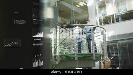 Discussing two colleagues wearing shirt and blouse holding tablet on mezzanine with data charts Stock Photo