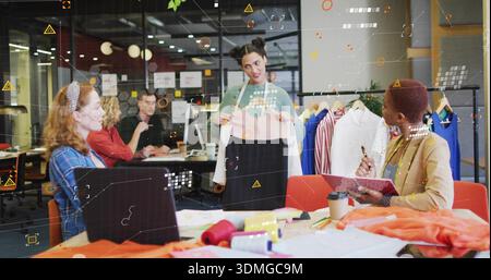 Holding presenter in green sweater and apron showing two-tone dress at studio with swatches, rack Stock Photo
